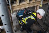 A person wearing safety equipment uses a tool while carrying a power supply backpack.