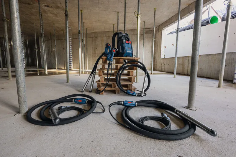 Construction site with two concrete vibrators and a backpack power supply on a pallet.