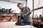 A person wearing safety equipment uses a cordless narrow crown stapler on fabric.