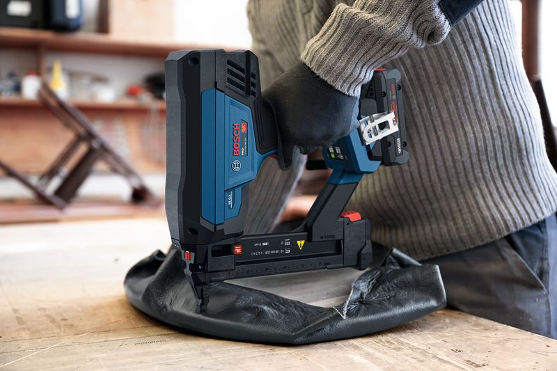 A person wearing safety equipment uses a cordless crown stapler to fasten upholstery.