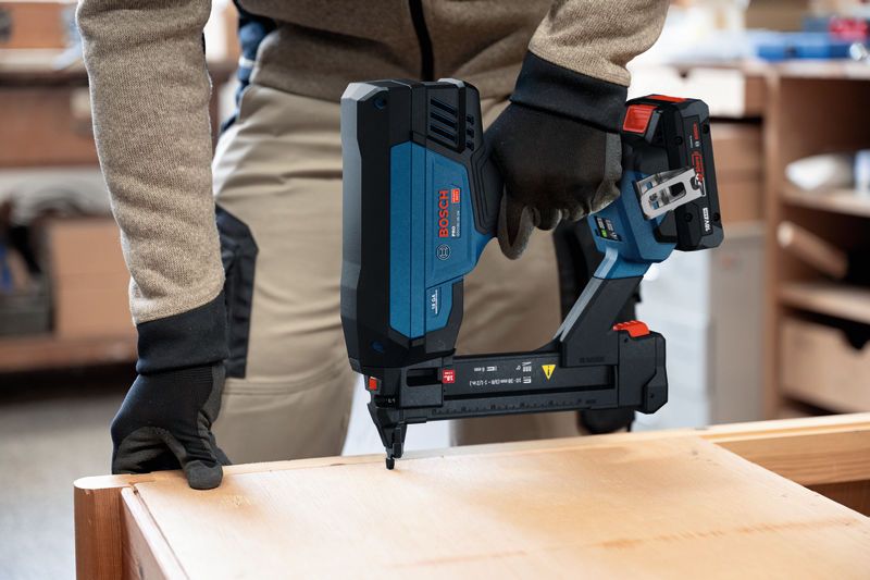 A person wearing safety equipment uses a cordless narrow crown stapler on wood.