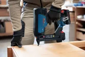 A person wearing safety equipment uses a cordless narrow crown stapler on wood.