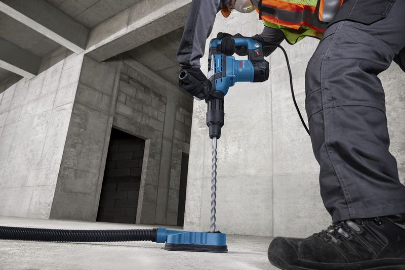 A person wearing safety equipment drills into concrete with a rotary hammer.