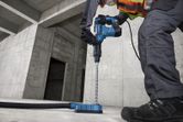 A person wearing safety equipment drills into concrete with a rotary hammer.
