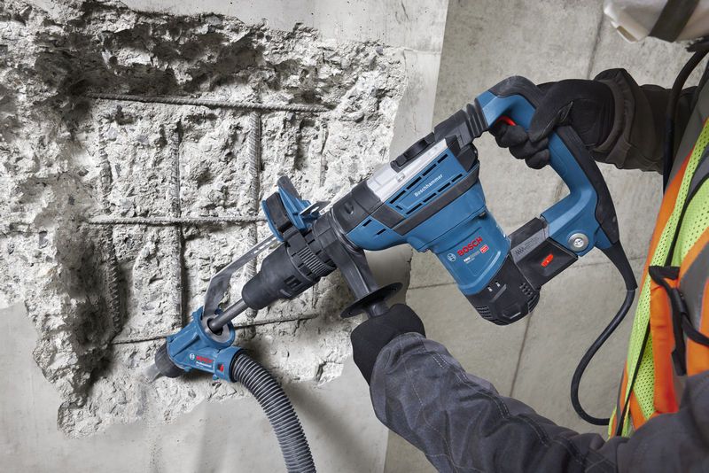 A person wearing safety equipment uses a rotary hammer to drill into concrete.