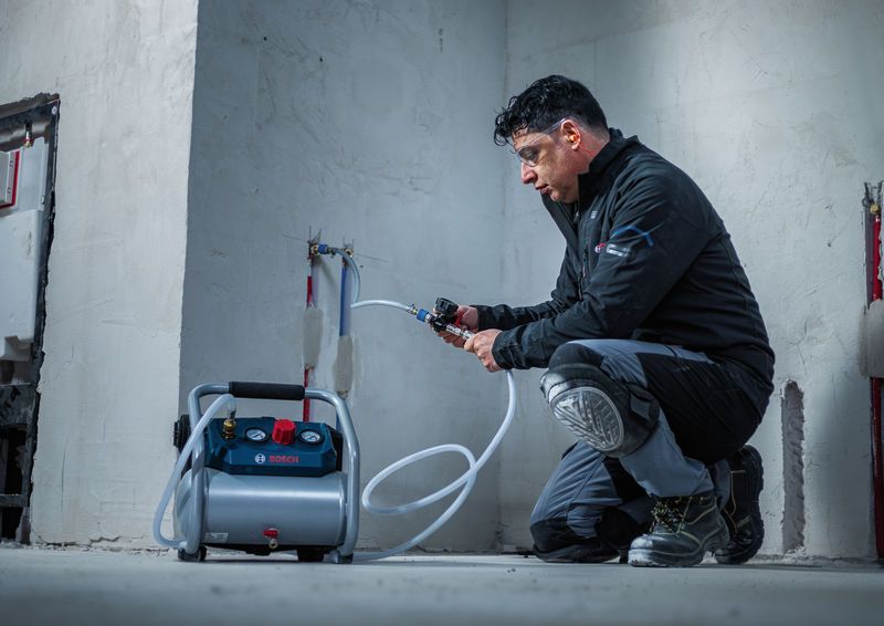 A person wearing safety equipment tests water pipes with a portable air compressor.