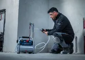 A person wearing safety equipment tests water pipes with a portable air compressor.