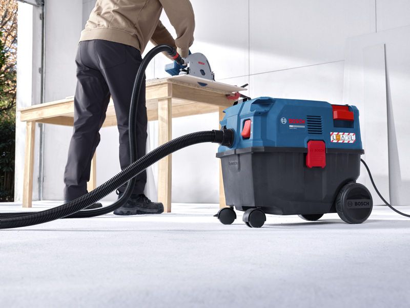 A person uses an all-purpose extractor connected to a saw while cutting wood.
