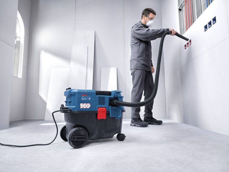 A person wearing safety equipment uses an all-purpose extractor to clean wall outlets.