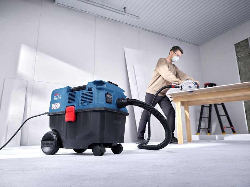 A person wearing safety equipment cuts wood on a table while using an all-purpose extractor.
