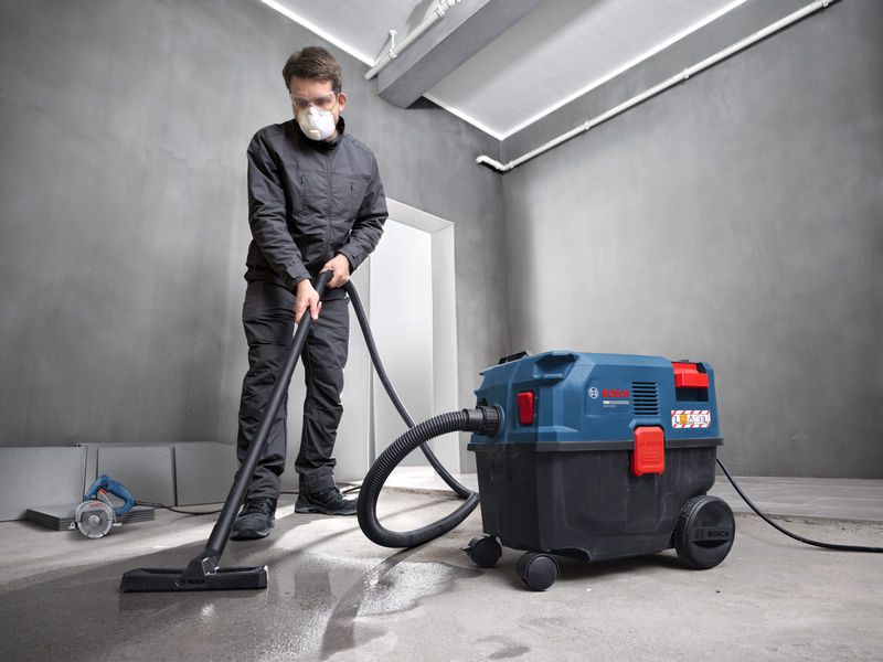 A person wearing safety equipment cleans a concrete floor using an all-purpose extractor.