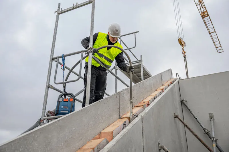A person wearing safety equipment uses a power tool on a concrete staircase at a construction site.