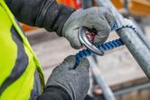 A person wearing safety equipment secures a climbing lanyard to scaffolding.