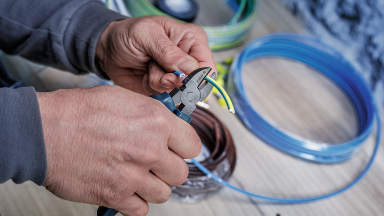 Person strips insulation from electrical wire using pliers.