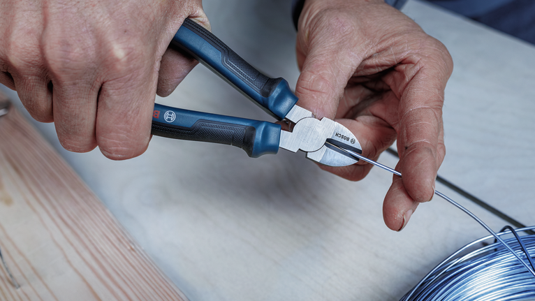 Person cuts metal wire with pliers at a workbench.