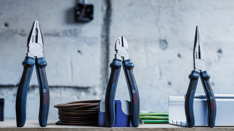 Three types of pliers are standing on a workbench in a workshop.