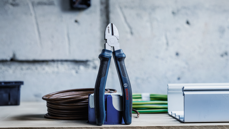 Cutting pliers standing on a workbench near coiled cables and a metal channel.
