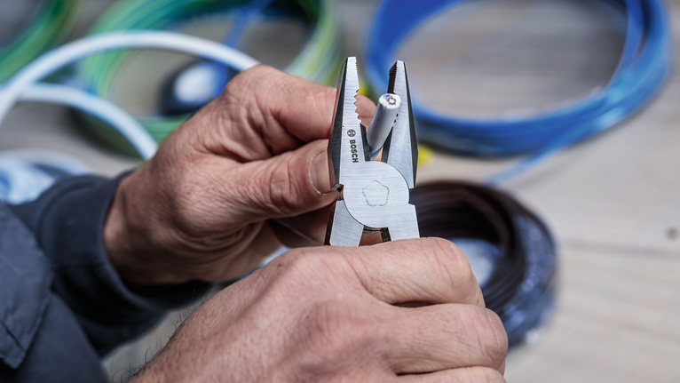 Person strips insulation from a wire using pliers.