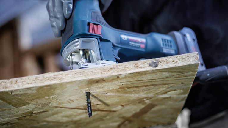Person wearing safety equipment uses a jigsaw to cut a wooden board.