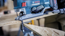 Person wearing safety equipment cuts wood with a jigsaw.