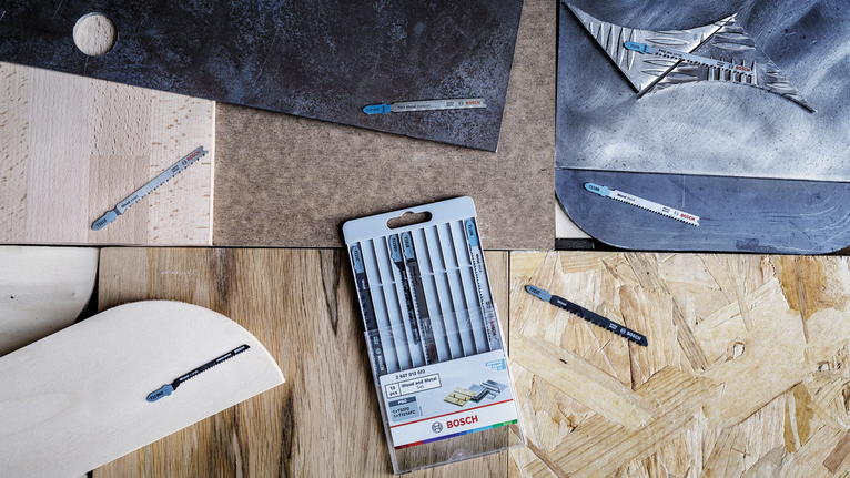 Jigsaw blades and packaging displayed on different wood, metal, and tile surfaces.