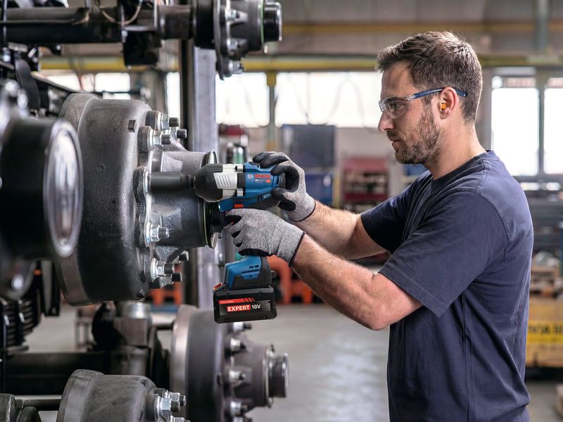 A person wearing safety equipment uses an impact wrench to tighten bolts on machinery.