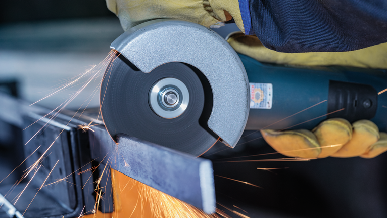 Person wearing safety equipment cutting metal with an angle grinder, sparks flying.