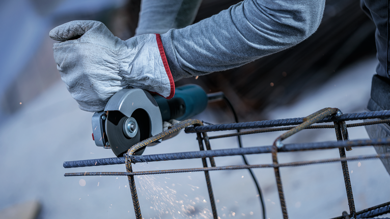 Person wearing safety equipment cuts metal rebar with an angle grinder.