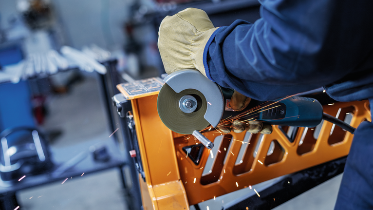 Person wearing safety equipment uses an angle grinder to cut metal, creating sparks.