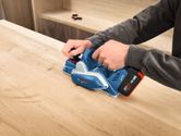 Person using a cordless planer to smooth a wooden surface.