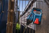 A blue and red power tool rests against a metal wire fence outdoors.