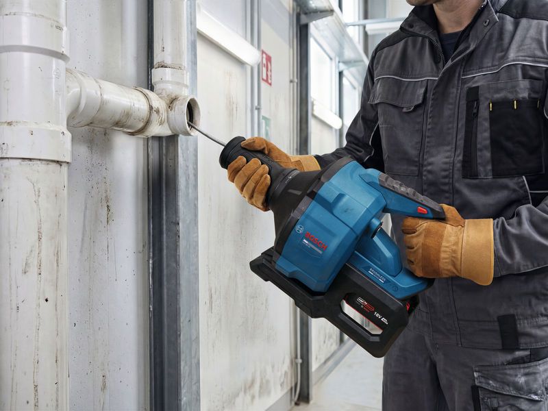 Person wearing safety equipment cleans a pipe with a cordless drain cleaning tool.