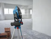 Portable jobsite fan on a tripod blows air in an empty room with construction bags.