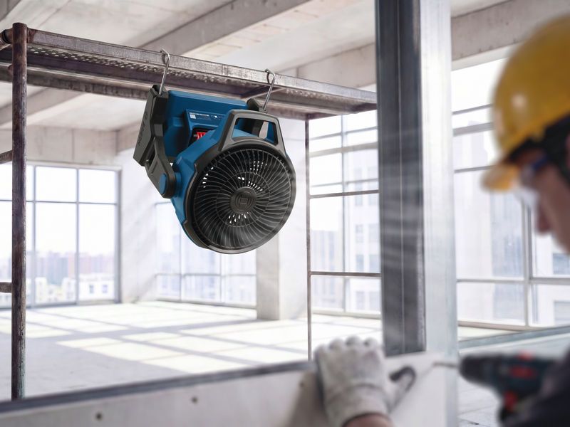 Portable jobsite fan hanging from a metal frame, person wearing safety equipment nearby.