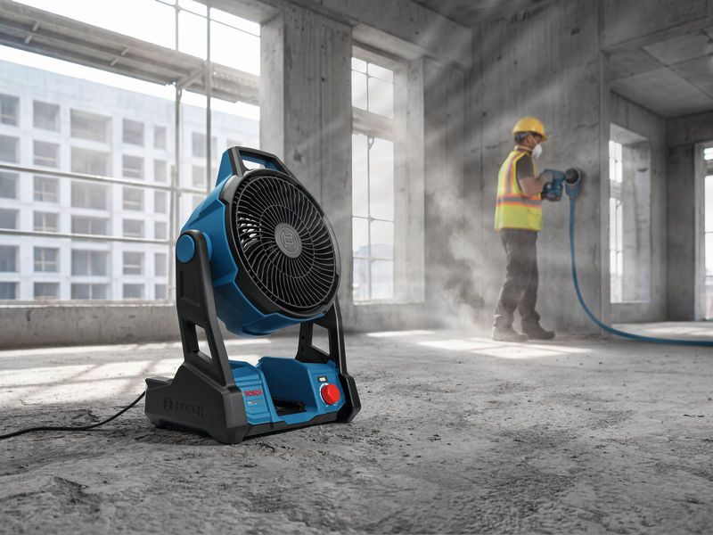 A worker wearing safety equipment grinds concrete while a portable fan operates nearby.