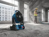 A worker wearing safety equipment grinds concrete while a portable fan operates nearby.