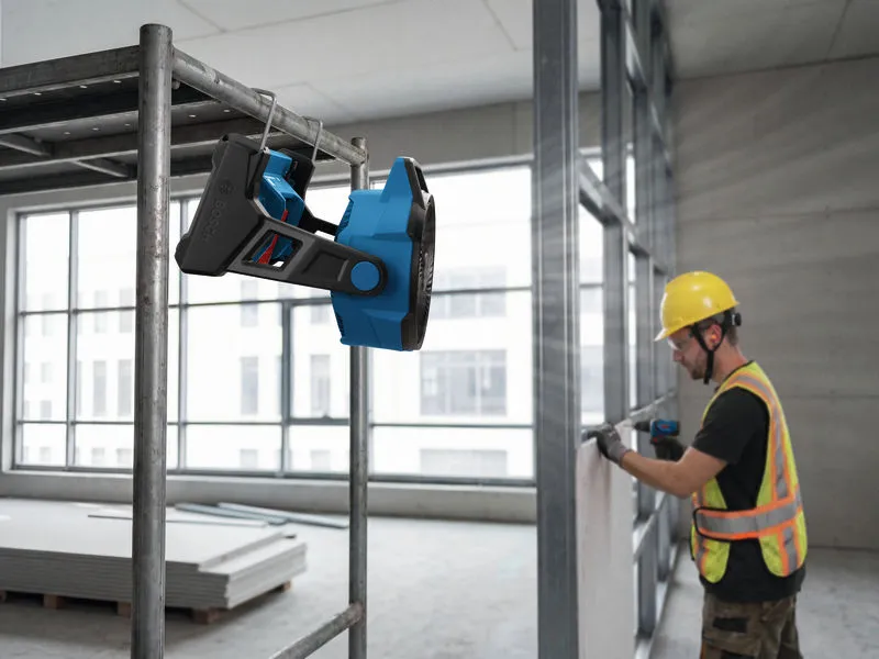 A person wearing safety equipment operates a power tool near a mounted portable fan.