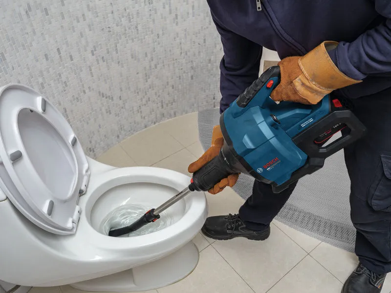 Person wearing safety equipment uses a power tool to unclog a toilet.