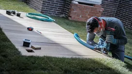 A person wearing safety equipment drills into a wooden panel on grass.