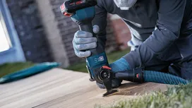 Person wearing safety equipment uses a power tool to cut a wooden board outdoors.