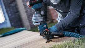 Person wearing safety equipment uses a power tool to cut a wooden board outdoors.