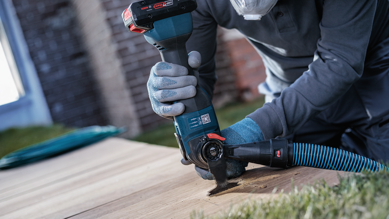 Person wearing safety equipment uses a power tool to cut a wooden board outdoors.