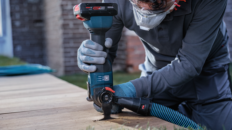 Person wearing safety equipment uses a cutting tool to cut wood outdoors.
