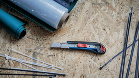 Utility knife placed on a workbench beside rolled plastic sheets and cable ties.