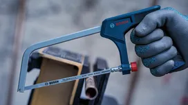 Person wearing safety equipment uses a hacksaw to cut a metal pipe.