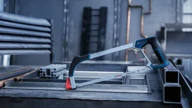 Hacksaw resting on a metal workbench in an industrial setting.