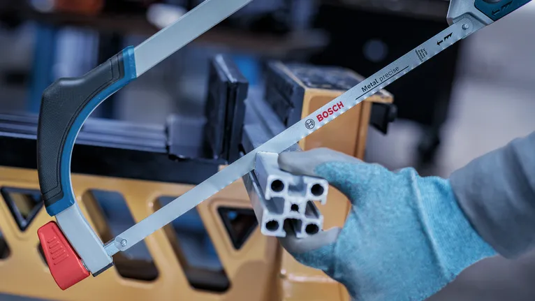 Person wearing safety equipment cutting a metal profile with a hacksaw.