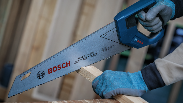 Person wearing safety equipment cuts wood with a hand saw.