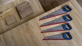Four hand saws with blue handles are arranged on a wooden workbench.