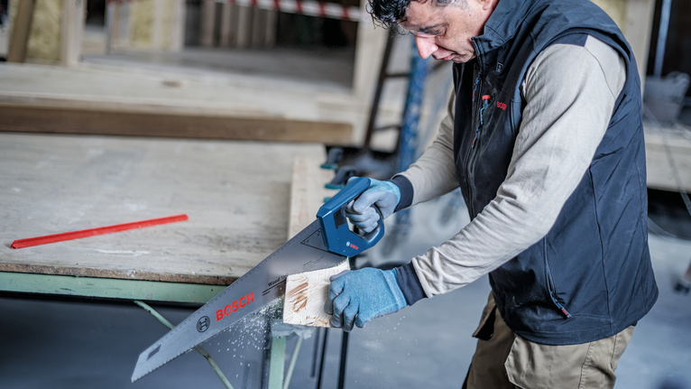 Person wearing safety equipment cuts wooden plank with a cordless saw.